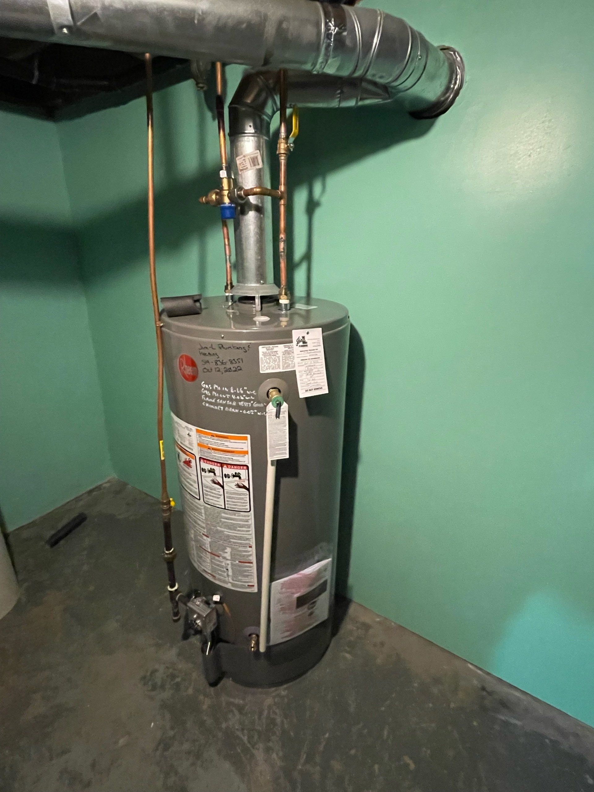 A water heater is sitting in a basement next to a green wall