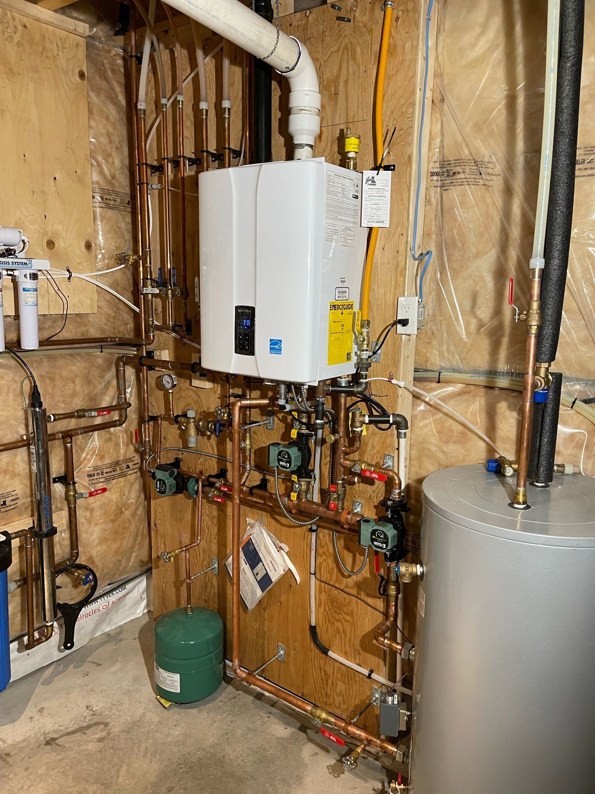 A water heater is sitting in a basement next to a water tank.
