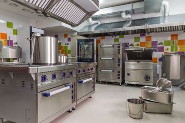 Commercial kitchen with stainless steel stoves, ovens, pots, and ventilation hoods