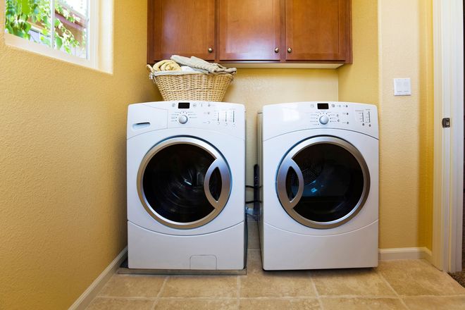 Laundry room with a white front-load washer and dryer beneath wooden cabinets and a small window.