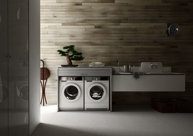 Modern bathroom with twin front-load washers under a sink and wood-paneled wall.