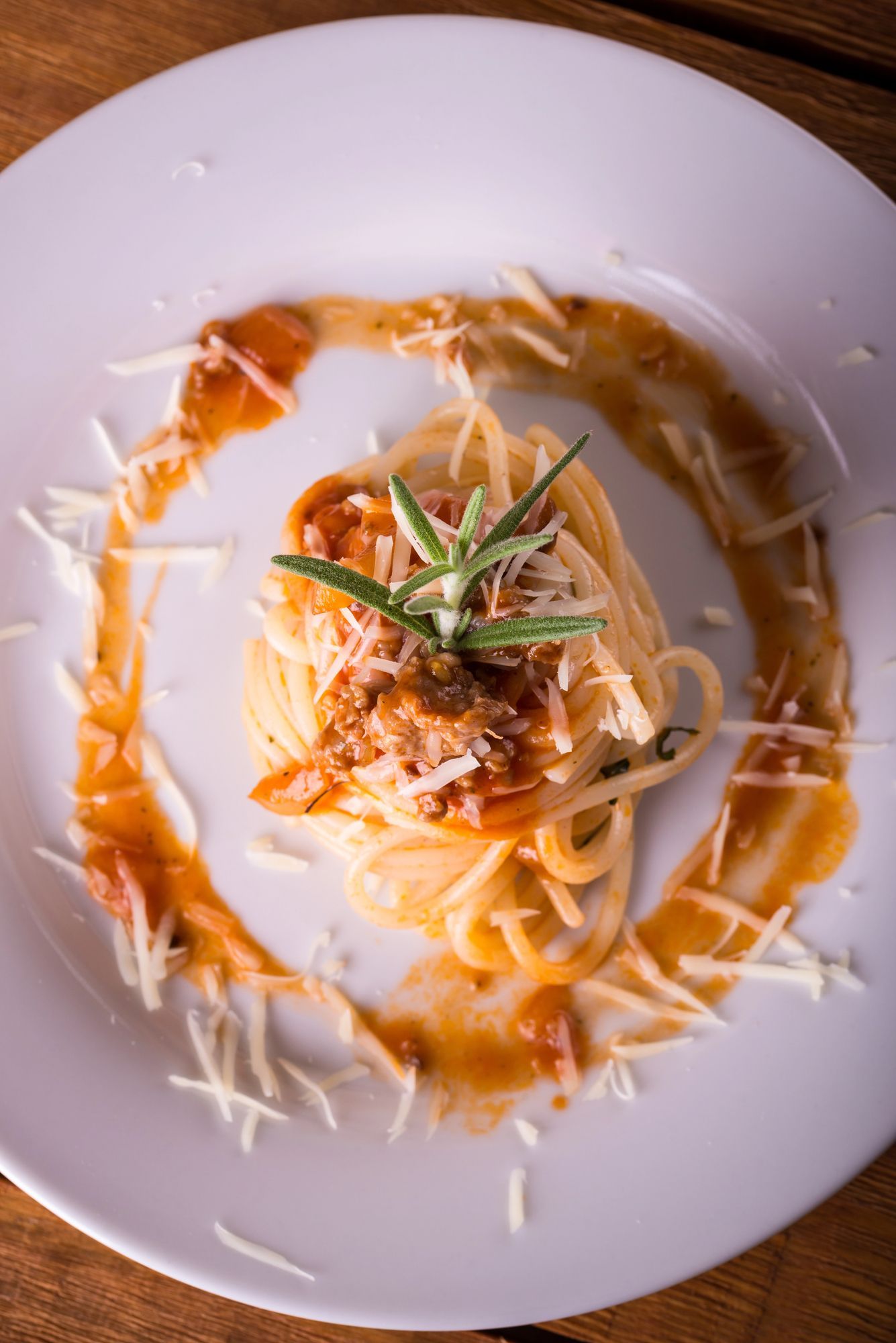 Piatto di spaghetti condito con salsa di pomodoro, formaggio e rametto di rosmarino, con salsa e formaggio disposti ad arte sul piatto bianco.
