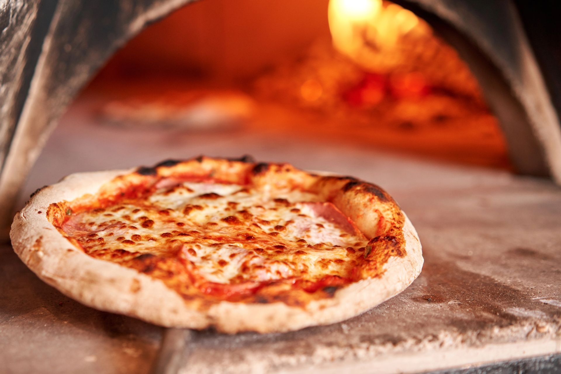 Pizza nel forno a legna. La pizza è dorata con formaggio fuso; il forno è caldo e arancione.