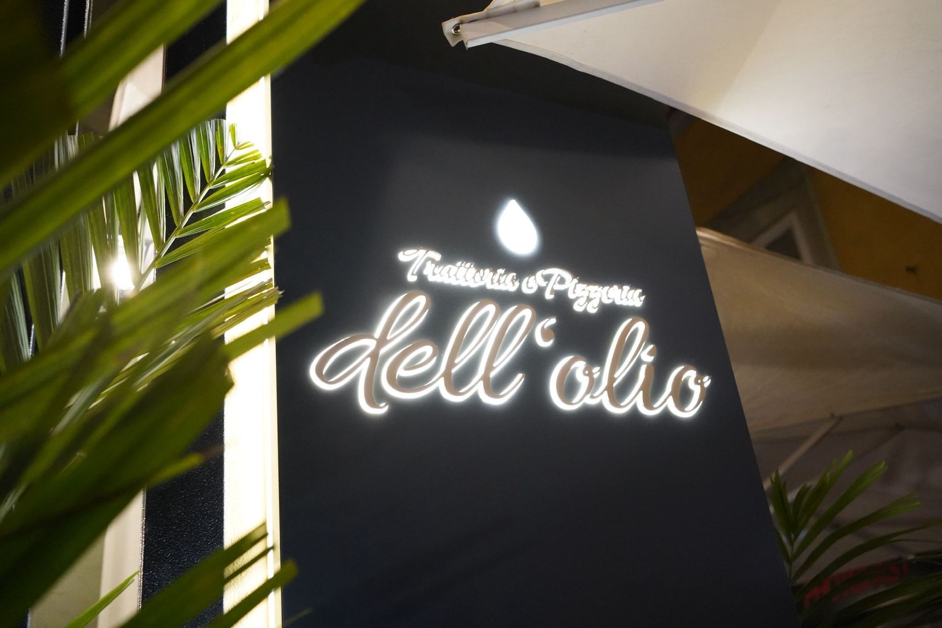 Tavolo del ristorante apparecchiato con tovaglia bianca, bicchieri da vino e condimenti, illuminato dalla luce del sole.