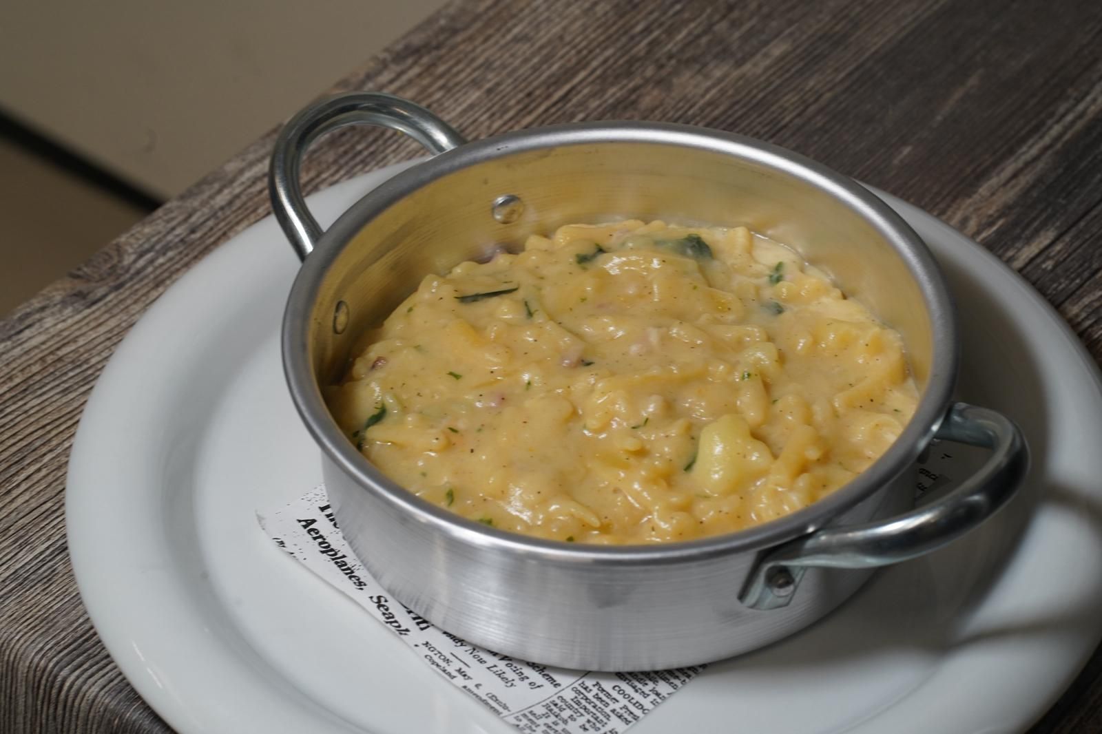 Chef con in mano un piatto di pasta guarnito con erbe aromatiche.