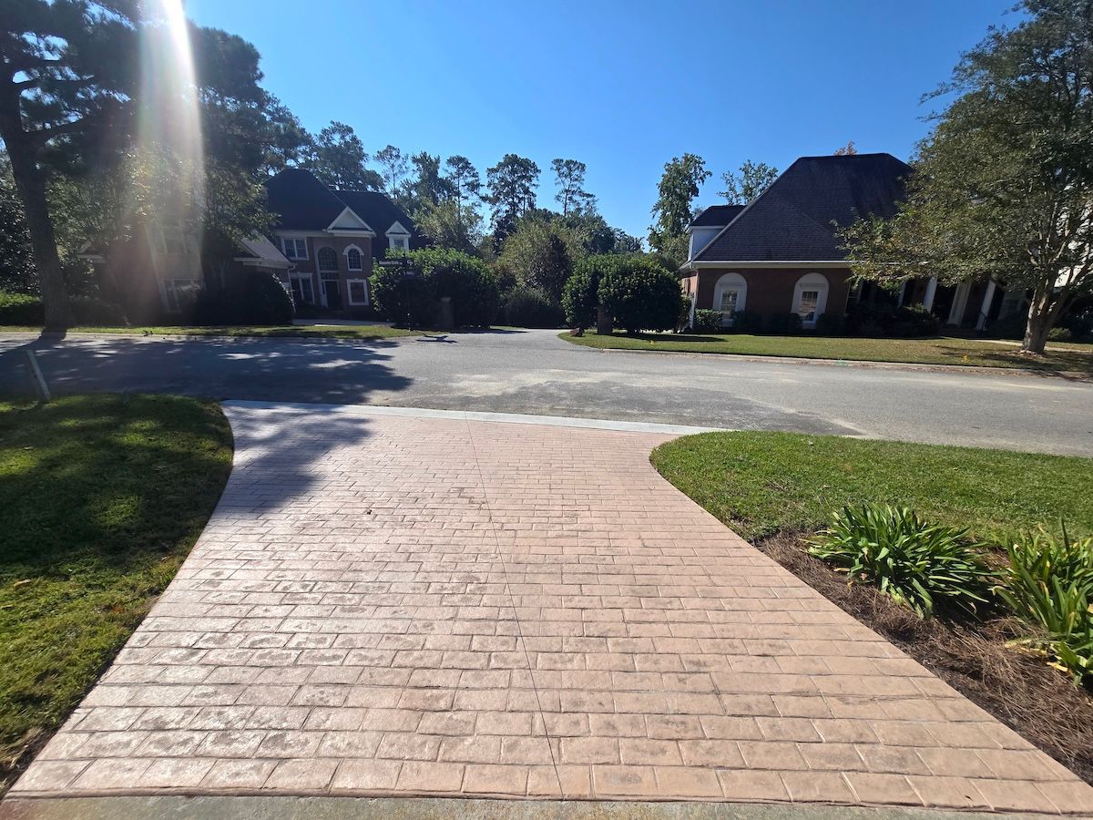 A stamped concrete driveway leads to a street in a suburban neighborhood on a sunny day.