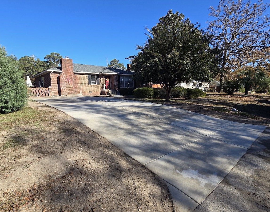 A brick house with a front chimney and a large concrete driveway set against a clear blue sky.