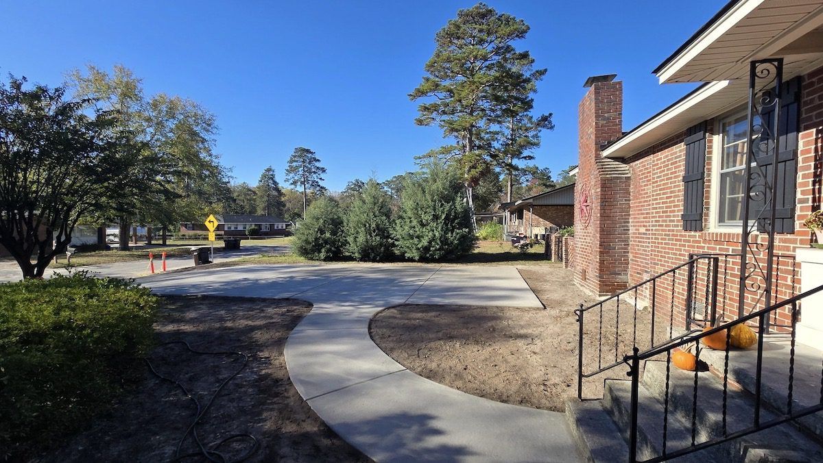 A brick house exterior with a new concrete sidewalk leading to the front porch under a clear blue sky.
