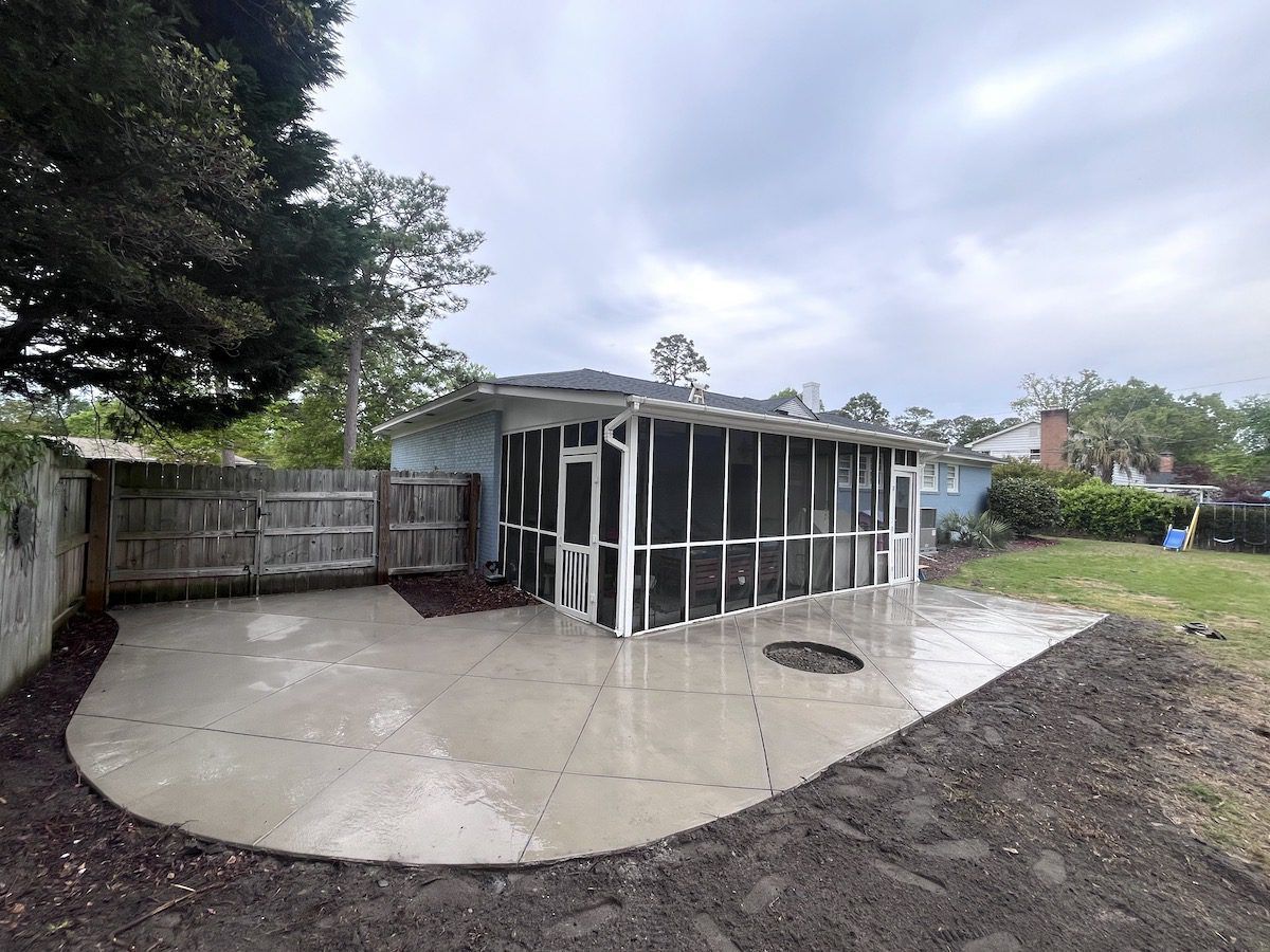 Newly poured concrete patio with a decorative grid pattern next to a screened-in porch and wooden fence in a backyard.