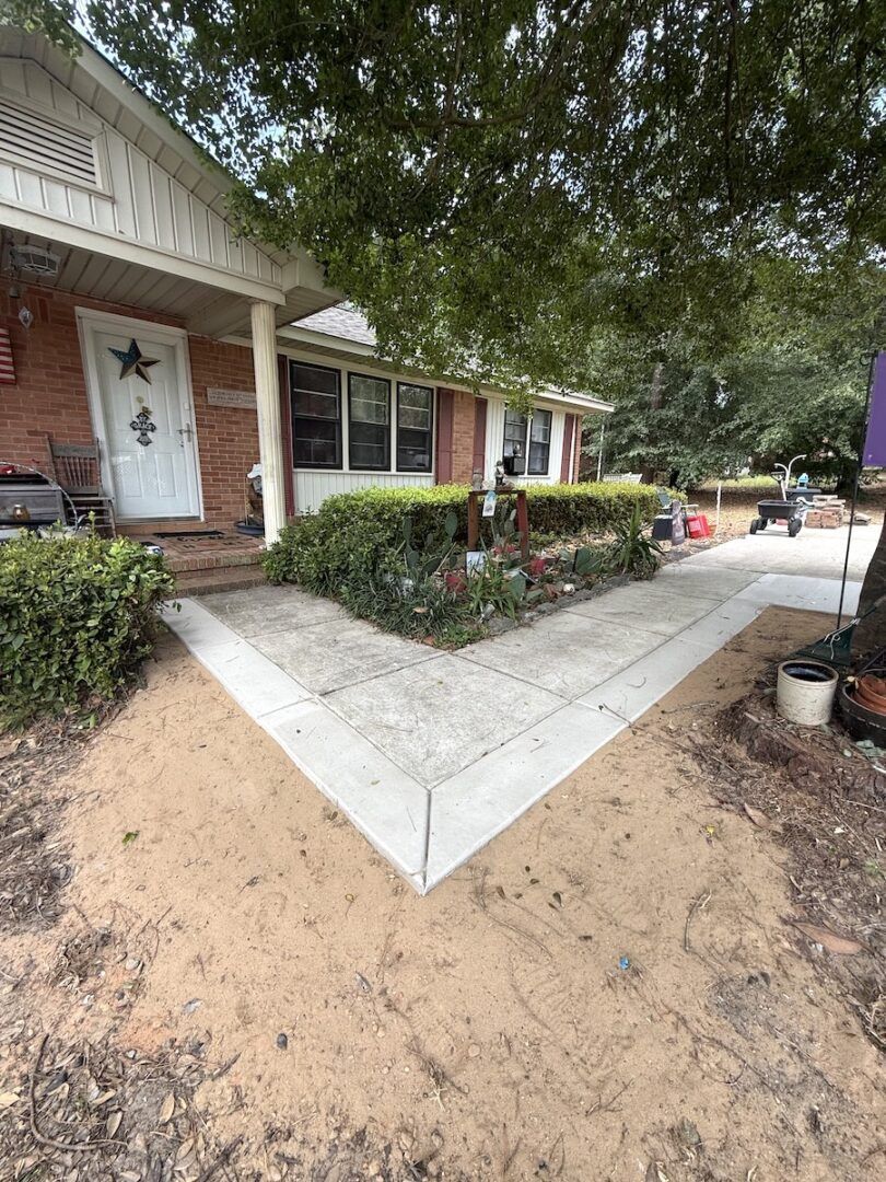 A white front door of a brick house with a newly poured concrete walkway and surrounding dirt landscaping.