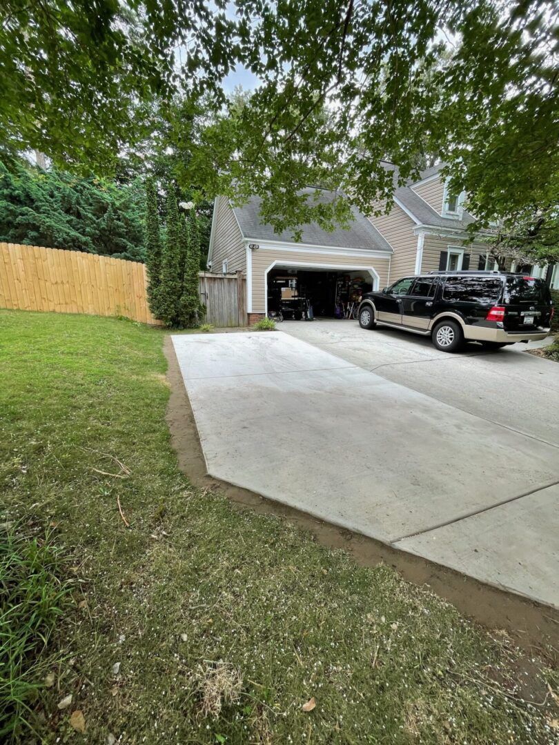 A new concrete driveway extension next to a grassy lawn, with a garage and a black SUV in the background.