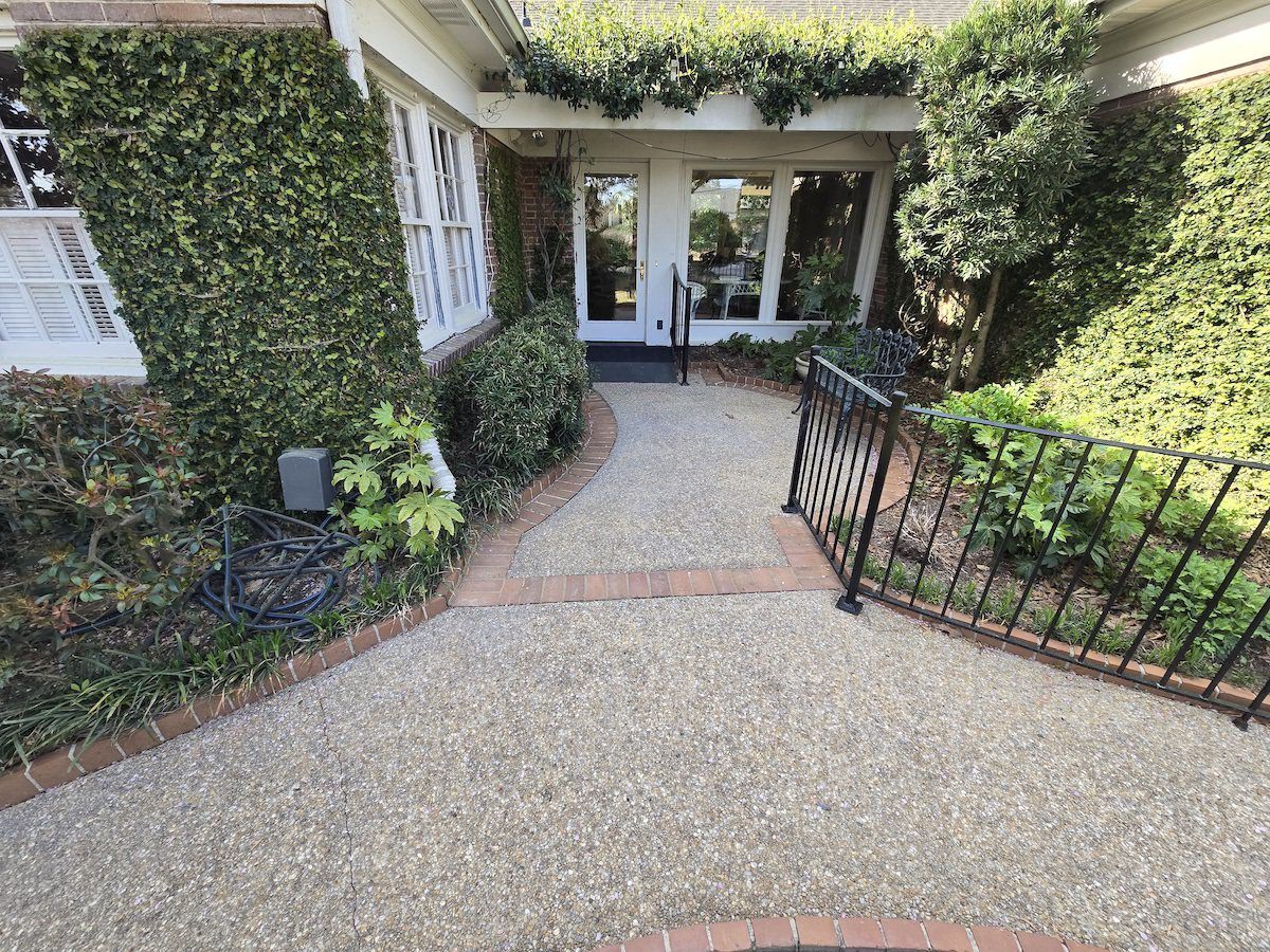 A gravel path lined with red bricks leads to a white front door, surrounded by lush green ivy and bushes.