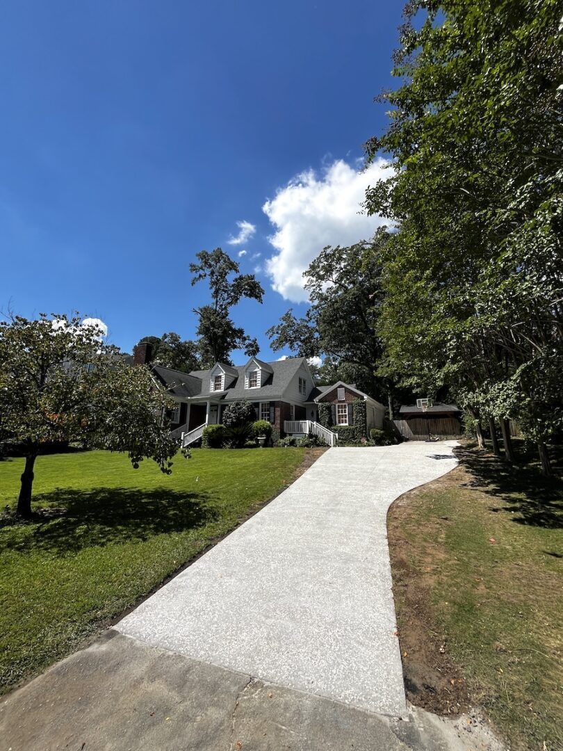 A house with a steep roof and dormer windows sits behind a freshly graveled driveway on a sunny day with blue skies.