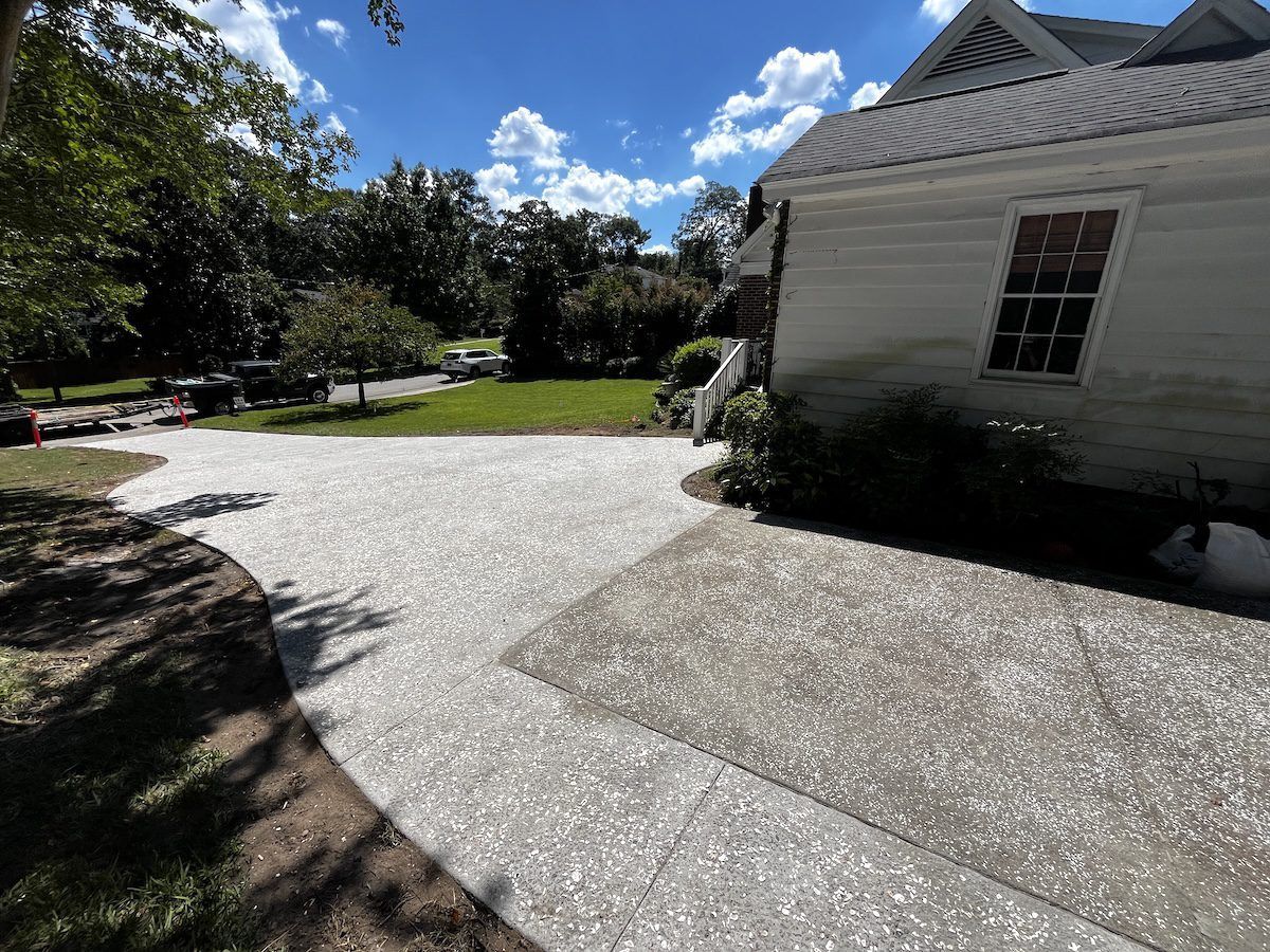 A light-colored shell-aggregate driveway leads toward a white building and green lawn under a sunny blue sky.