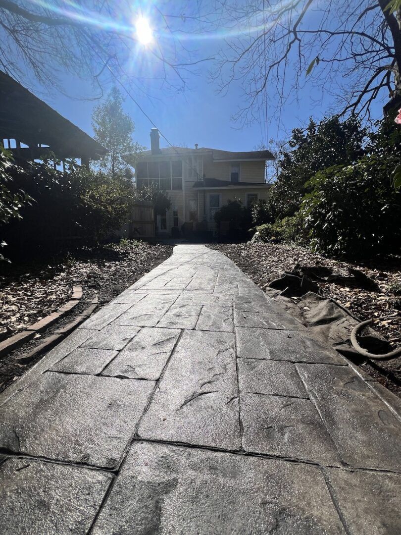 A low-angle view of a grey patterned stone walkway leading toward a house on a sunny day.