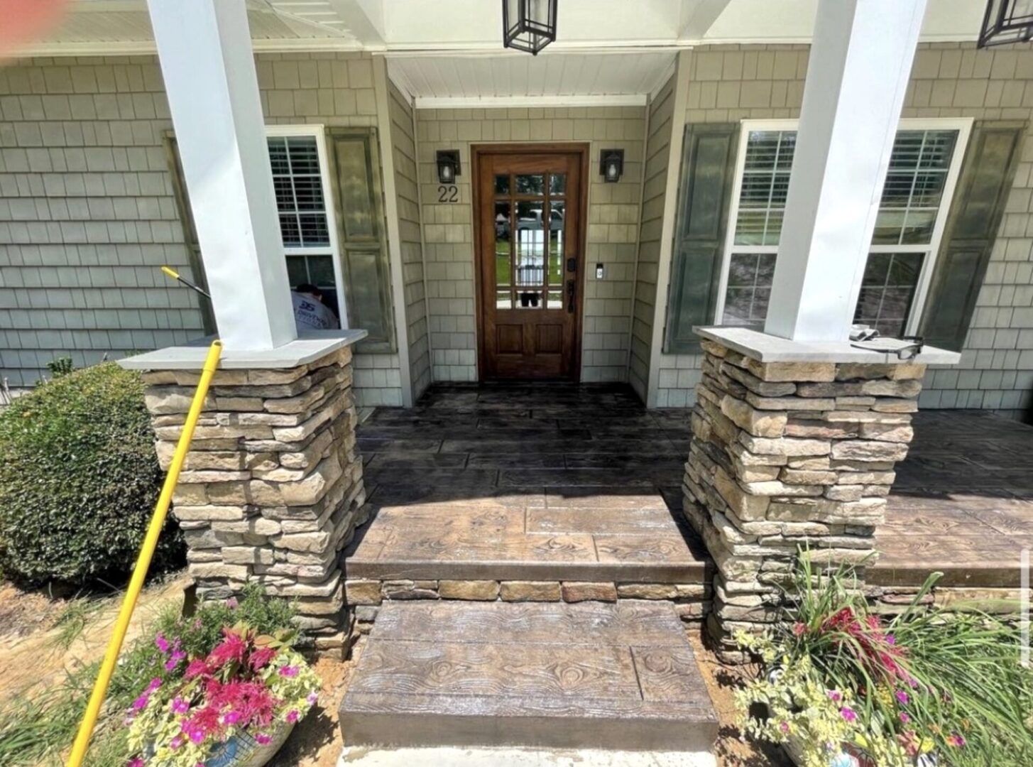 A front porch with stone-base columns and steps leading to a wooden front door, flanked by windows with shutters.