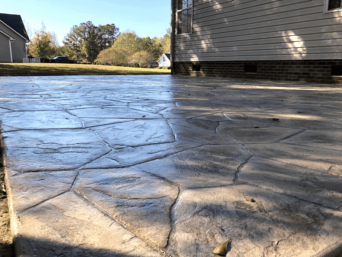 A newly installed stamped concrete patio with a gray flagstone pattern next to the side of a house.
