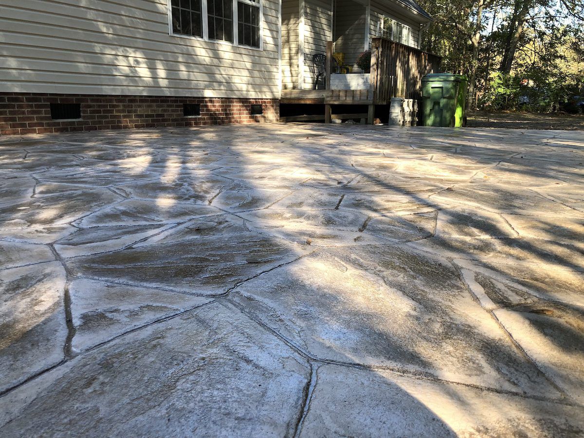 A patio with light-colored, irregular stone-patterned concrete stamps, located outside a residential home.