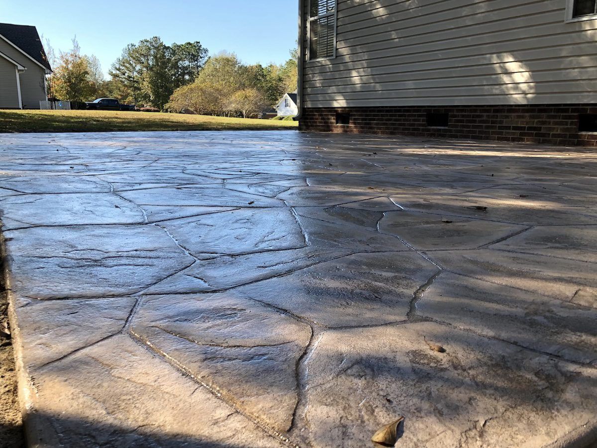A stamped concrete patio featuring a flagstone pattern, located next to the exterior wall of a house.