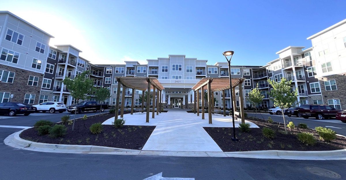 A multi-story apartment complex with stone and siding exterior, featuring a central courtyard with wooden pergolas.