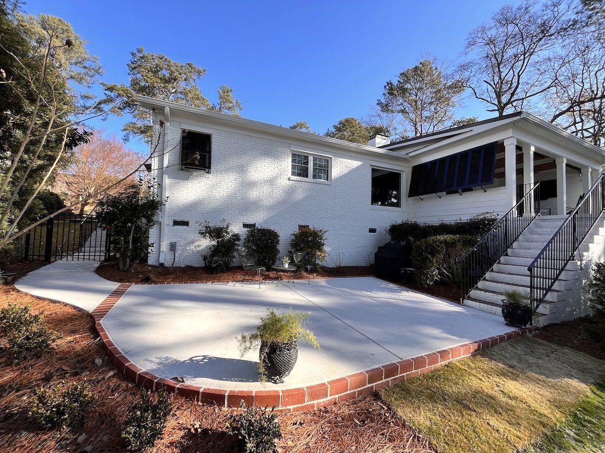 White house exterior with a curved concrete patio, red brick border, and stone steps leading to a covered porch.