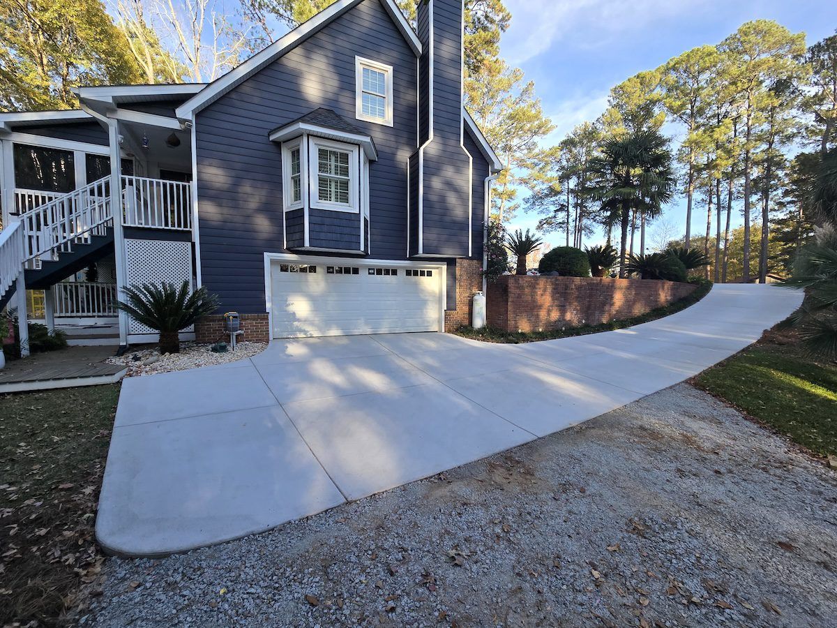A dark blue house with a white garage door, a concrete driveway, and a stone retaining wall against a wooded background.