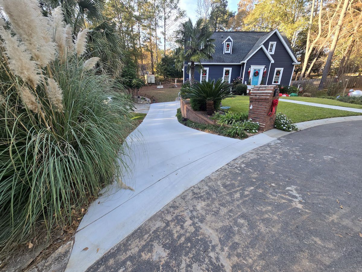 A paved driveway leads to a dark blue house with a brick mailbox near the street and tall ornamental grasses on the left.