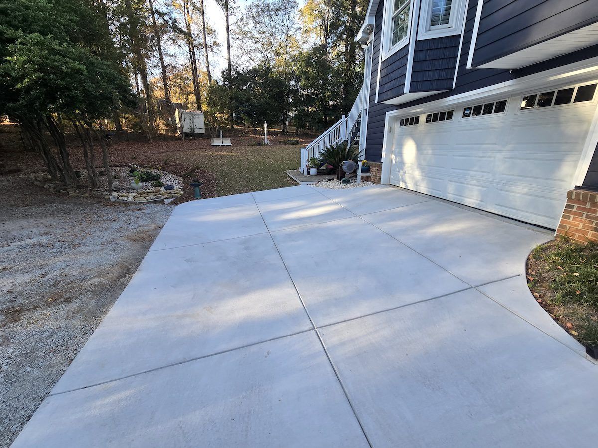 A newly poured, smooth concrete driveway extending from a dark blue house with a white garage door.