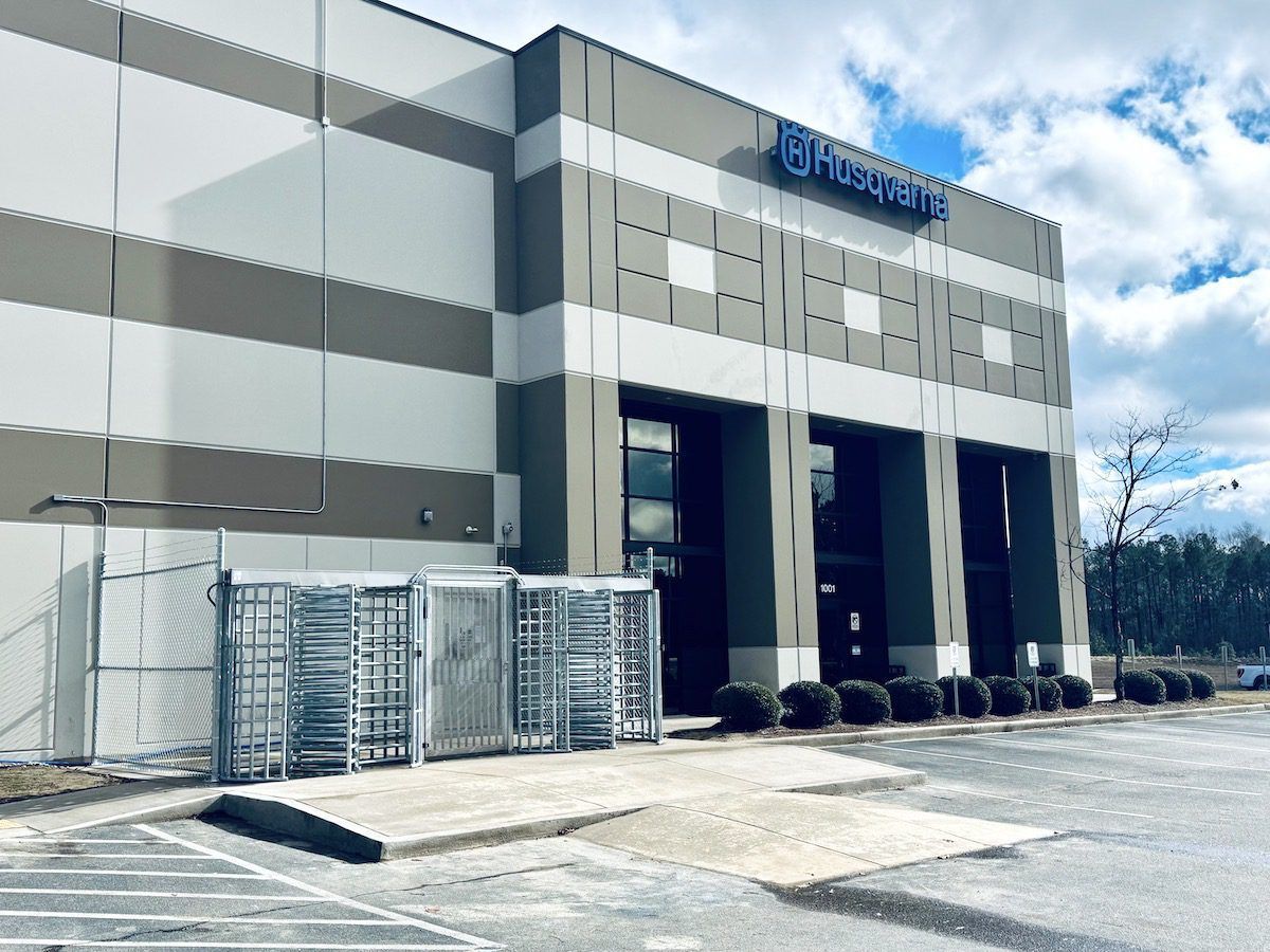 An exterior view of a Husqvarna warehouse building featuring a metal security turnstile gate at the entrance.