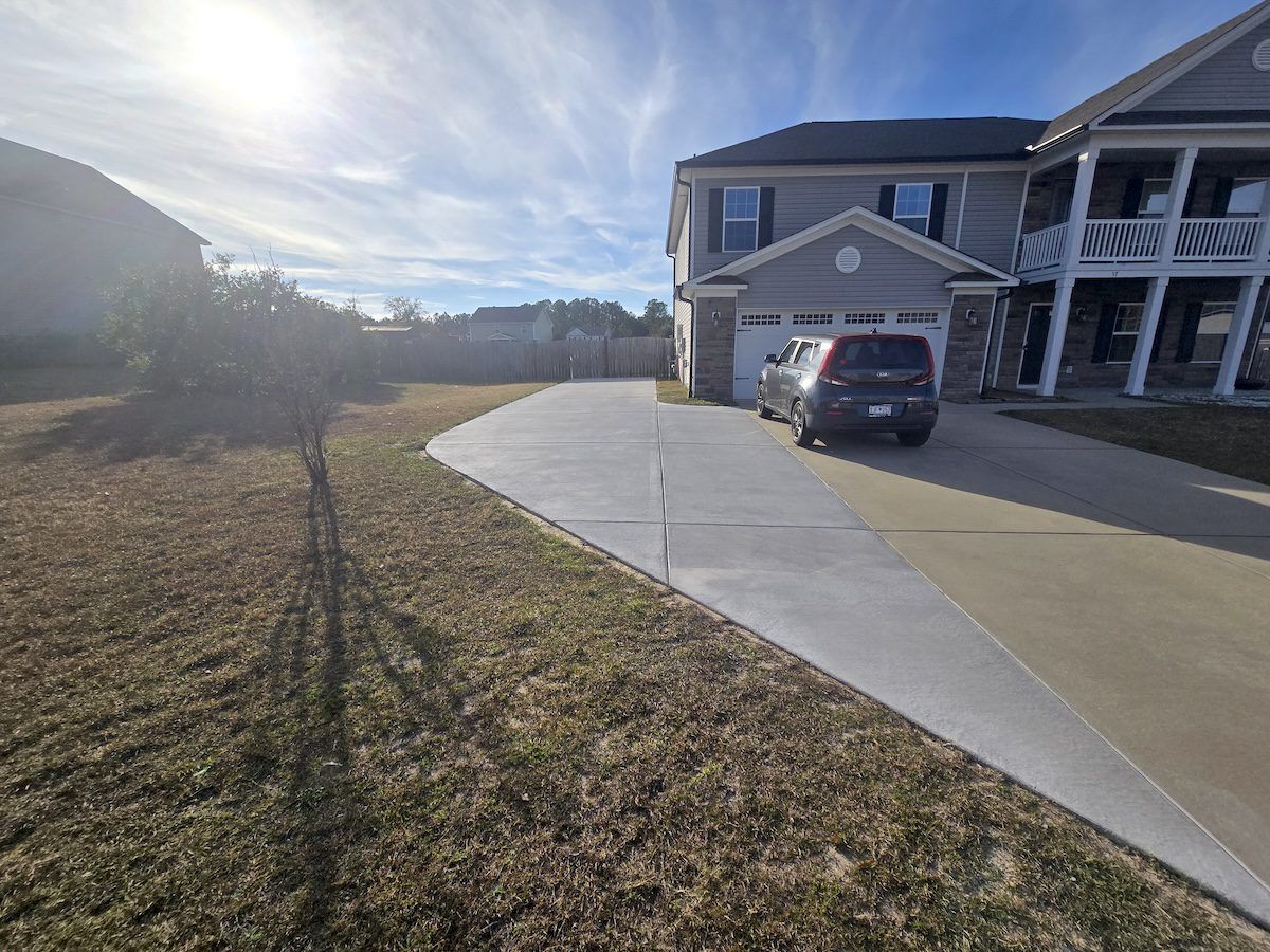 A modern gray house with a concrete driveway extending into a lawn under a bright, sunny sky.