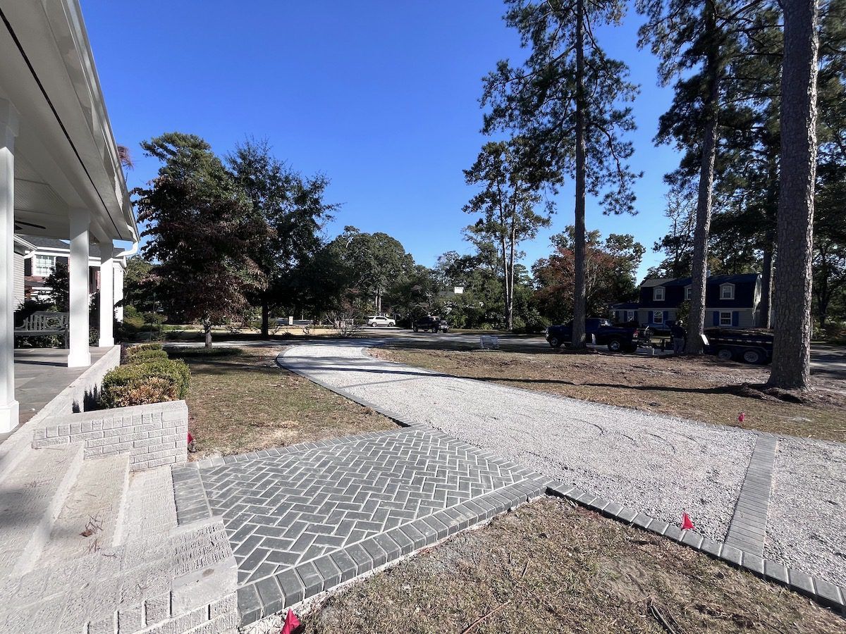 A stone walkway with a herringbone-patterned landing leads from a porch across a yard toward a house under a clear sky.