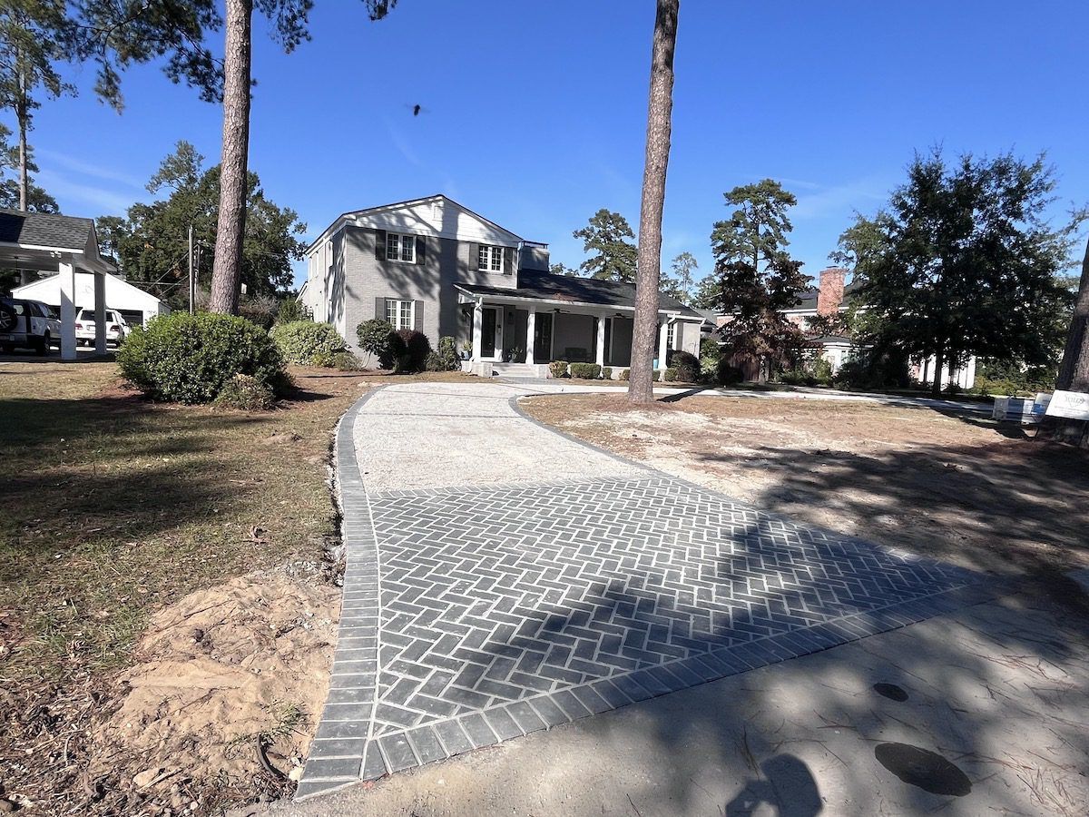 A brick-edged paver driveway leading to a two-story suburban house on a sunny day.
