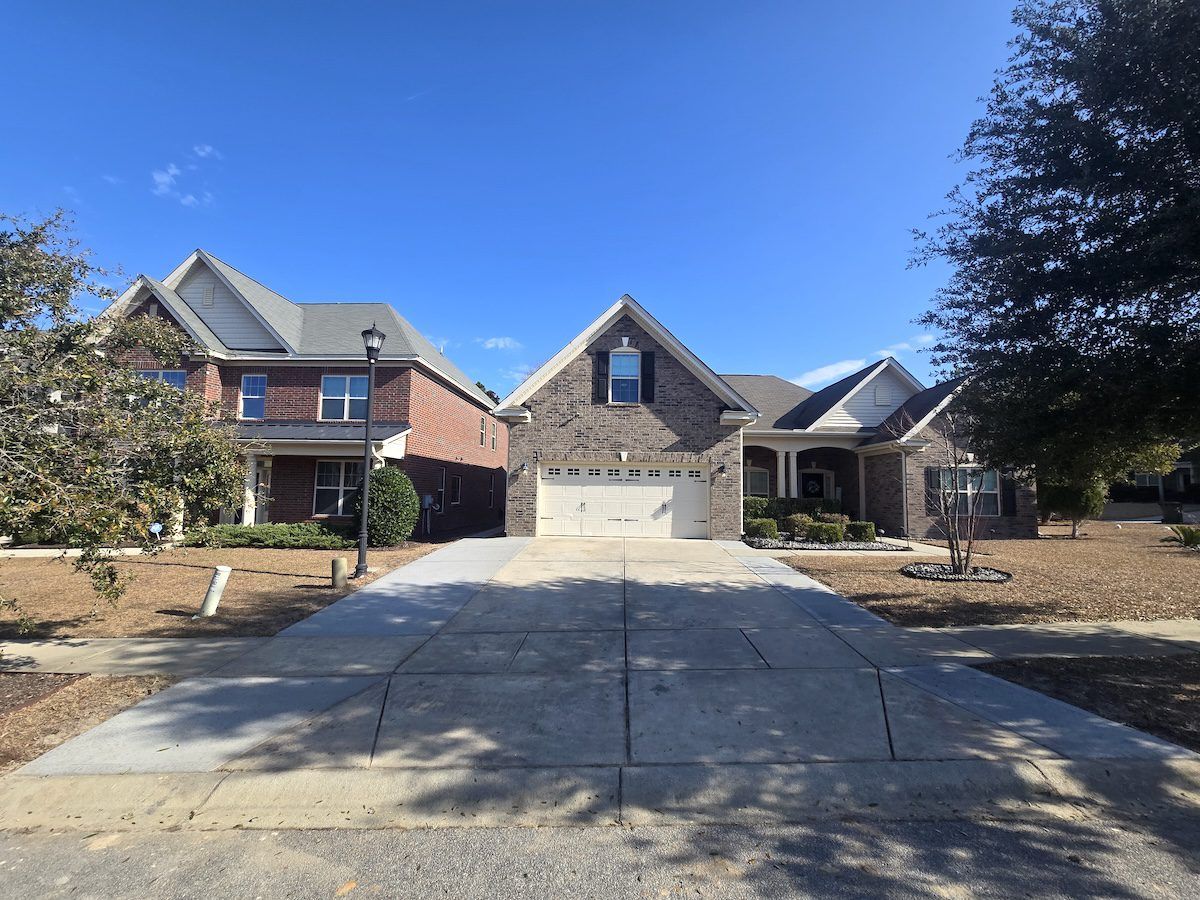 A two-story brick house with a front-facing garage and concrete driveway under a clear blue sky.