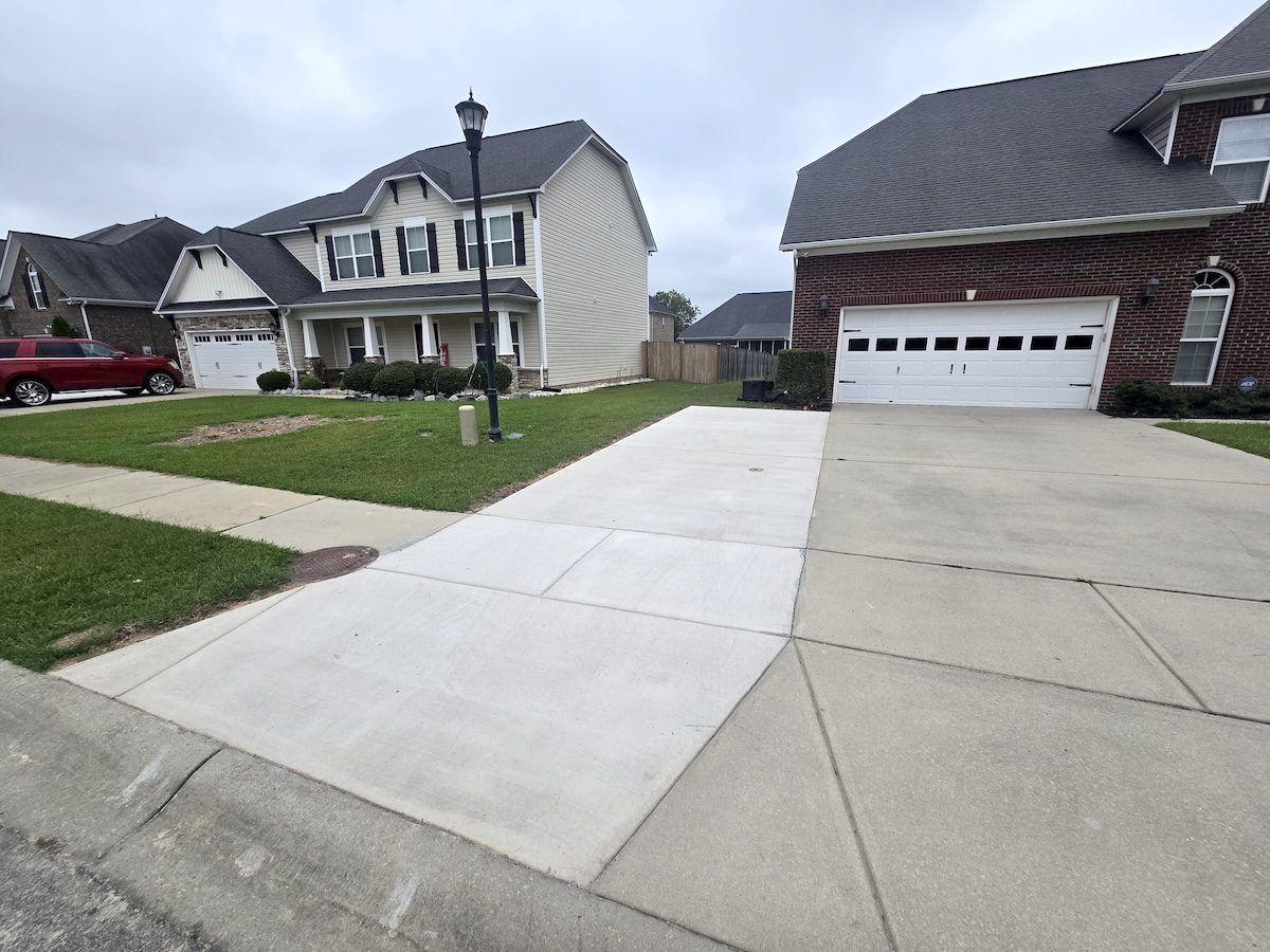 A wide residential driveway shows a freshly poured, light-colored concrete extension adjacent to an older, stained section.