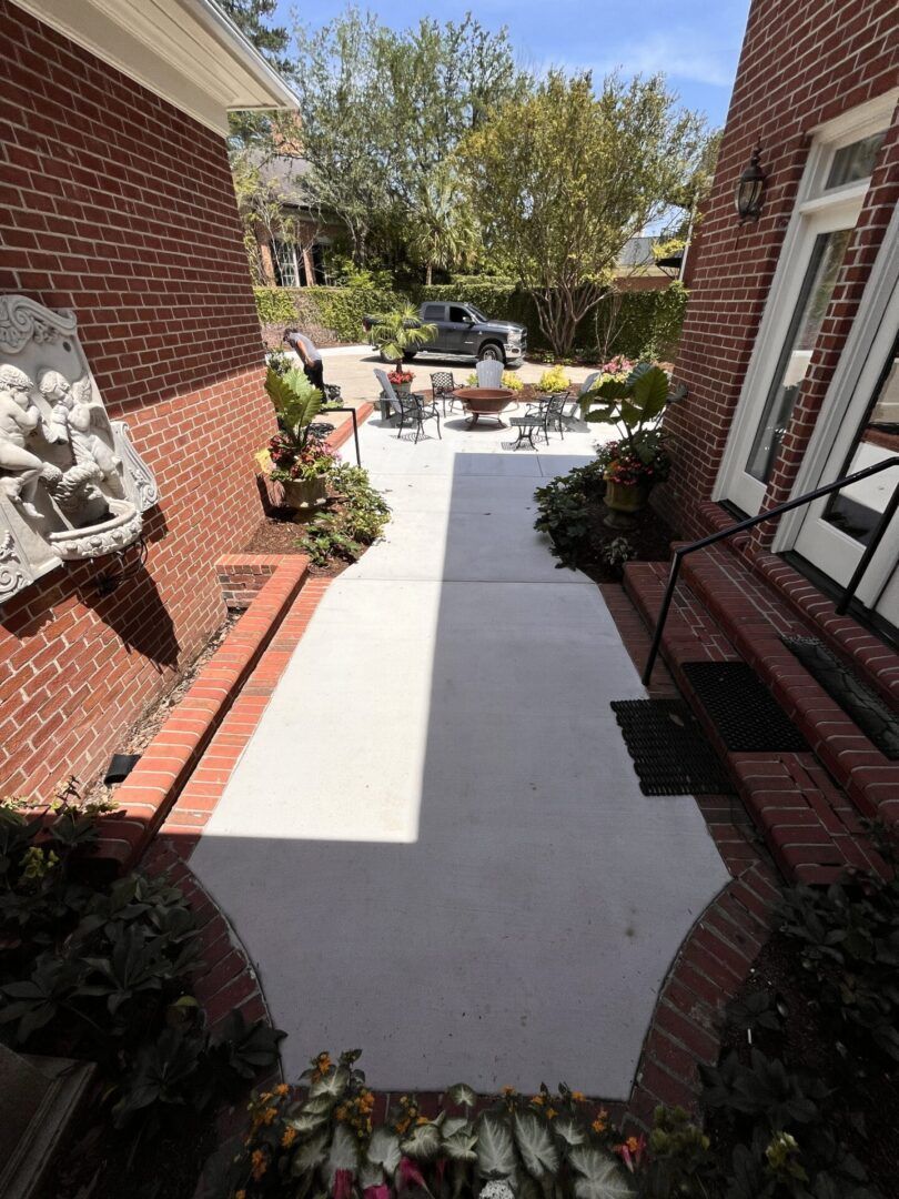 A sunlit brick patio walkway between two brick building walls, leading to a small outdoor seating area with a table.