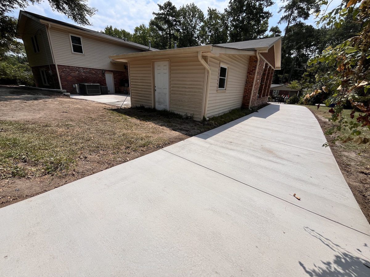 A light-colored house with a brick accent and a newly poured concrete driveway leading to the side entrance.
