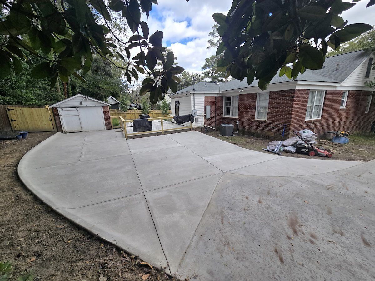 A newly poured concrete driveway and patio area beside a red brick house and small white garage.
