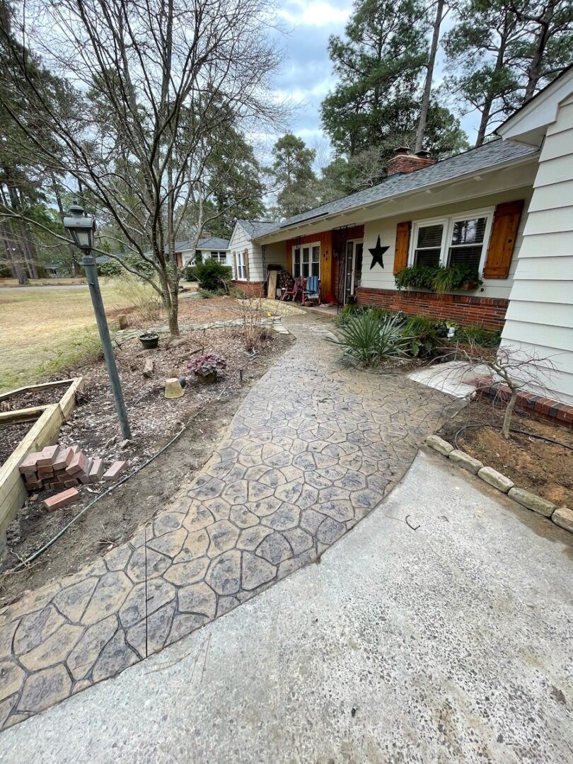 A stamped concrete walkway leads to the entrance of a house with white siding and a wood-trimmed porch.