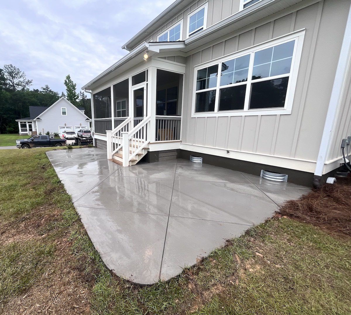 A light-colored house with a screened porch and a fresh concrete patio with a diagonal scored pattern.