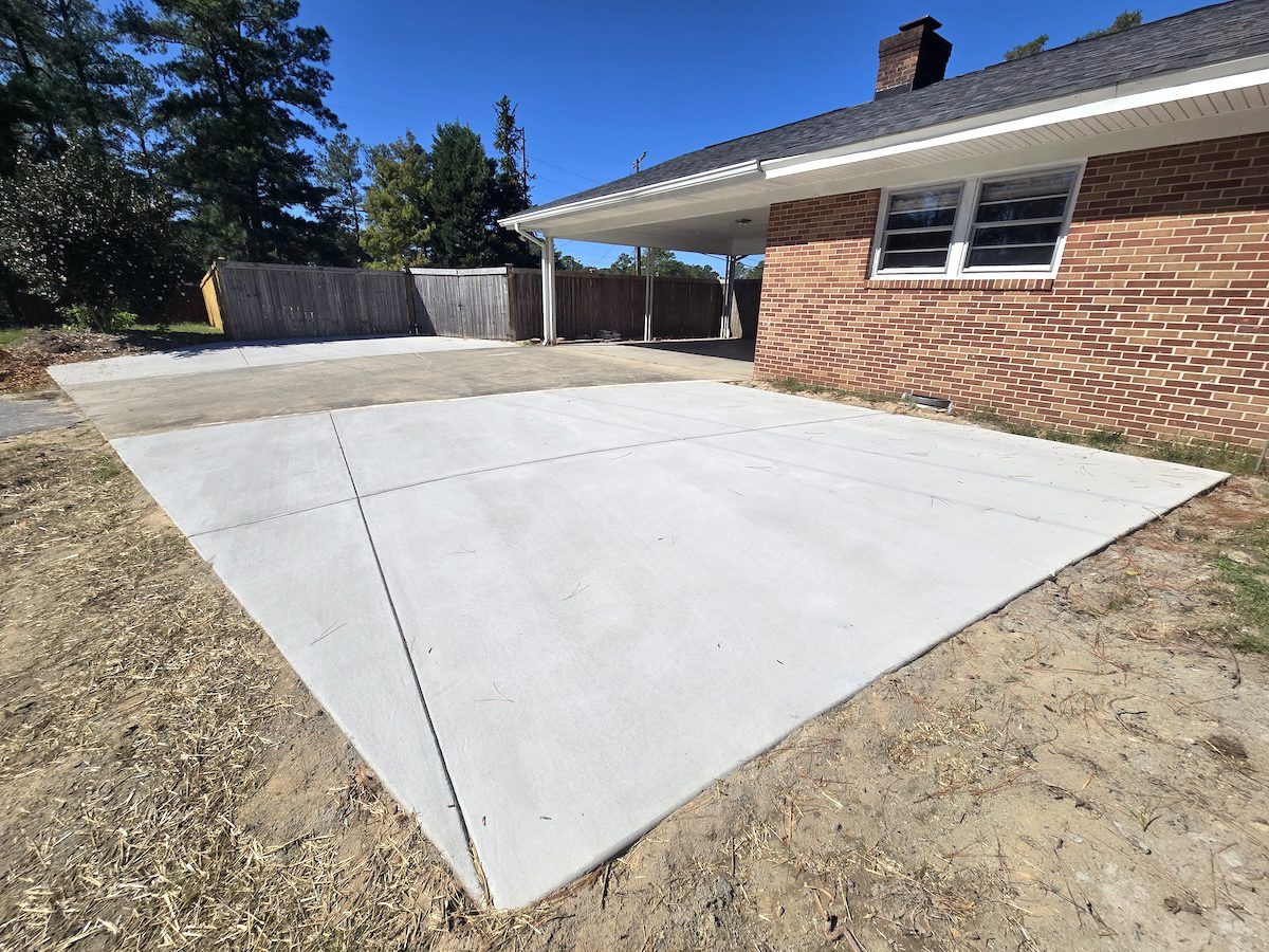 A view of a home with a large, newly poured light-gray concrete driveway slab situated next to an older concrete section.