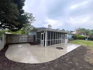 A backyard featuring a newly poured concrete patio with a diamond-scored pattern adjacent to a screened-in porch.