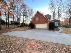 A two-story red brick house with a two-car garage at the end of a wide concrete driveway on a sunny day.