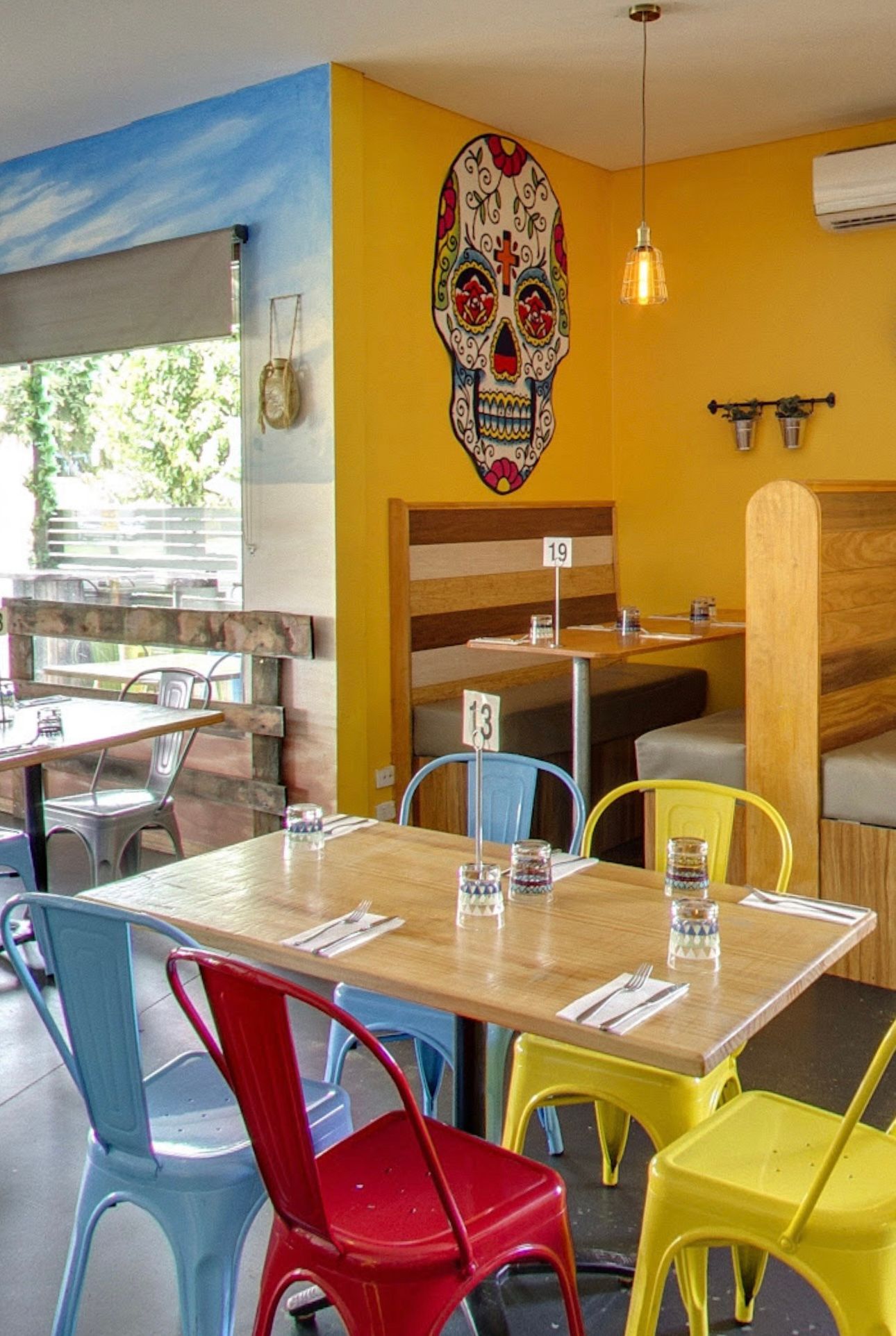 A brightly colored Mexican restaurant interior with a skull mural and colorful chairs.