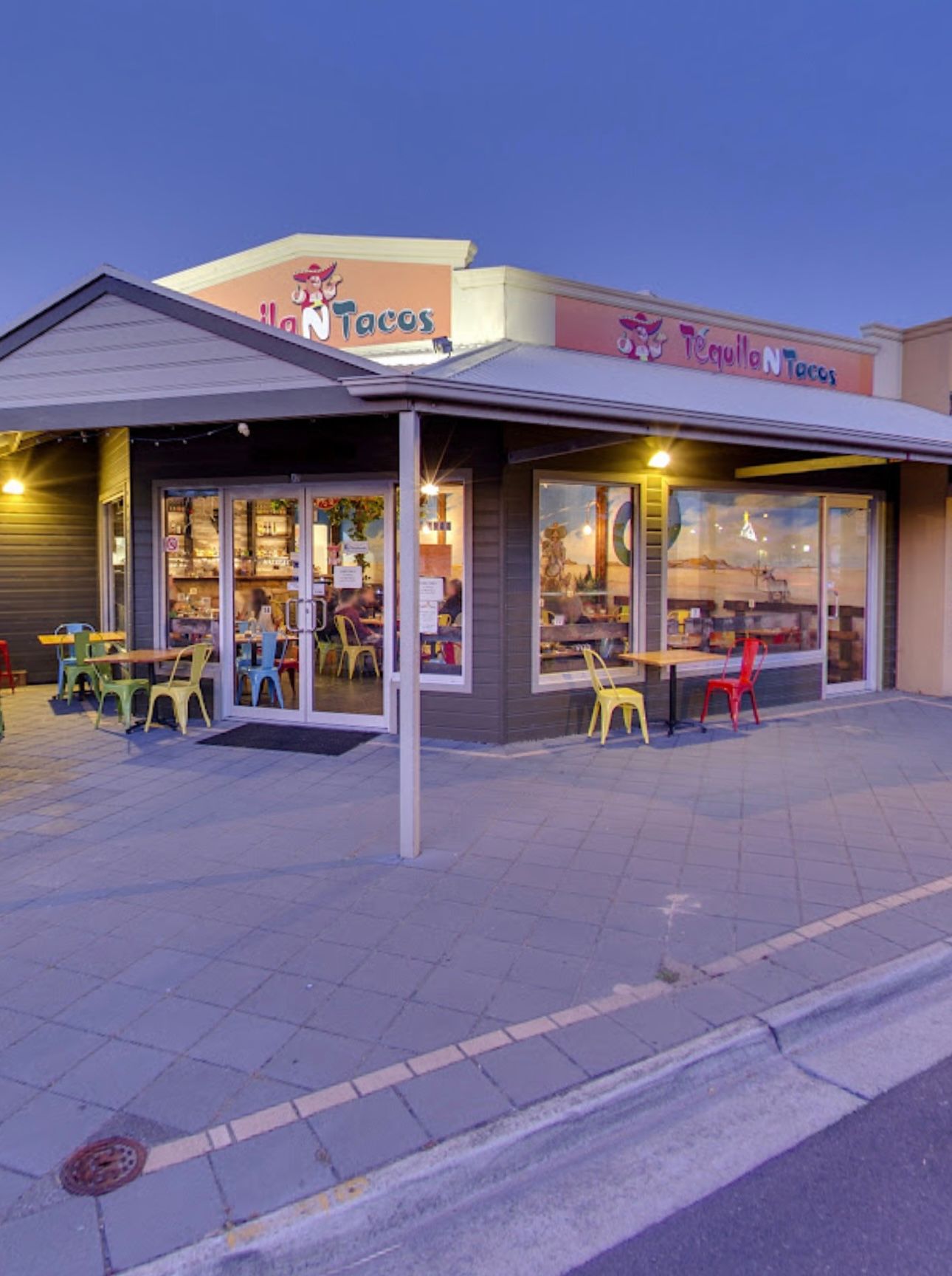 Exterior of a Fuzzy's Taco Shop restaurant with colorful chairs and windows.