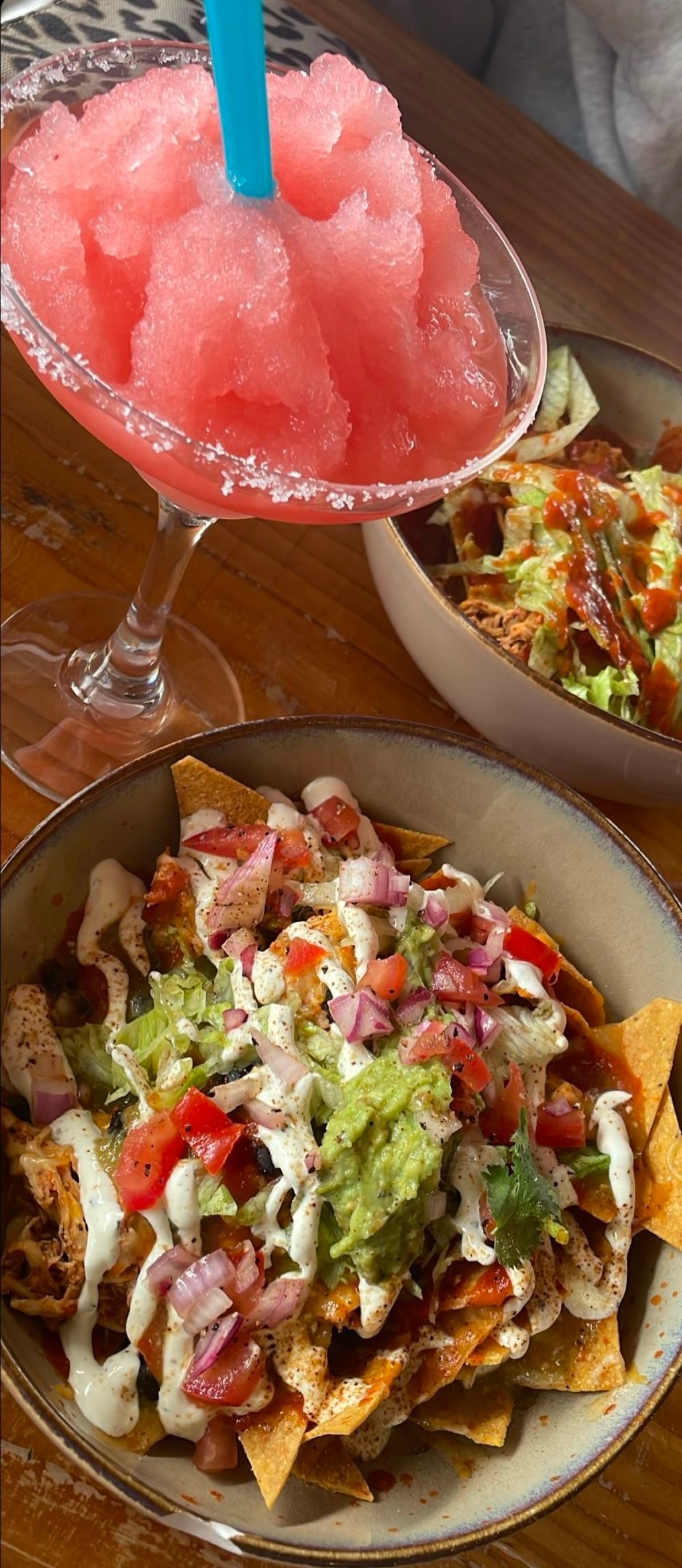 A margarita glass with a pink slushy and nachos topped with guacamole, and other ingredients.