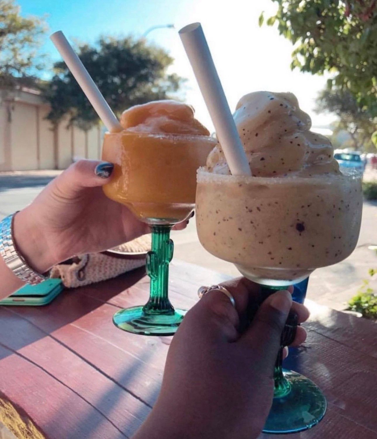 People toasting with colorful cocktails, garnished with fruit, outdoors.