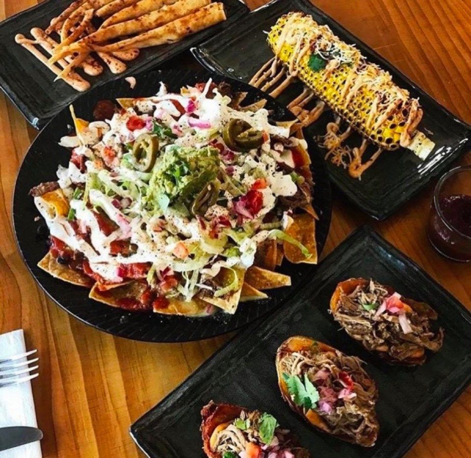 Plate of nachos with guacamole, corn on the cob, and pulled pork