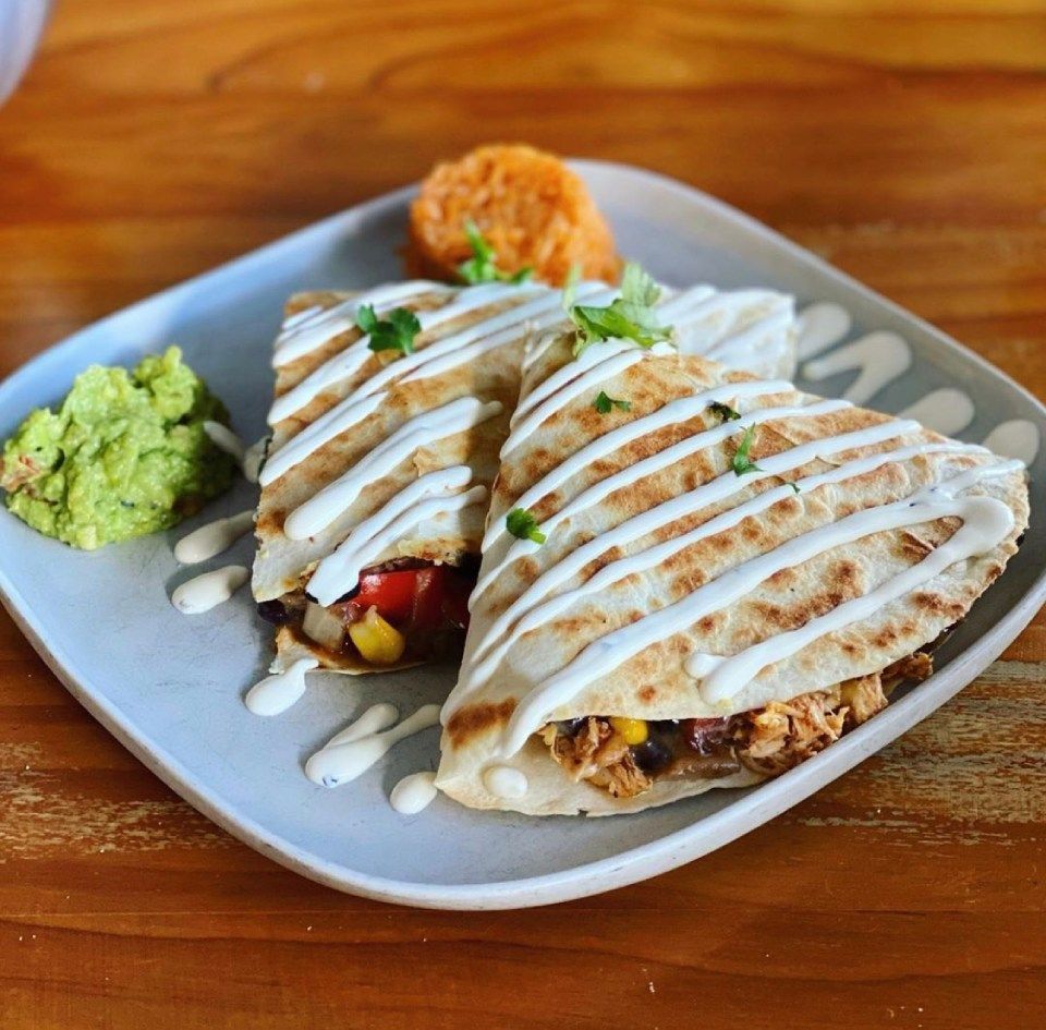 Quesadillas with sauce drizzle, guacamole, and rice on a plate.