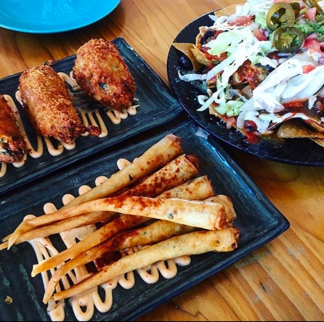 Plates of food, including fried appetizers, and nachos, on a wooden table.
