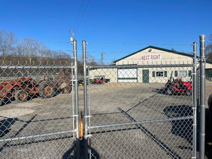 A chain link fence surrounds a building with tractors parked in front of it.
